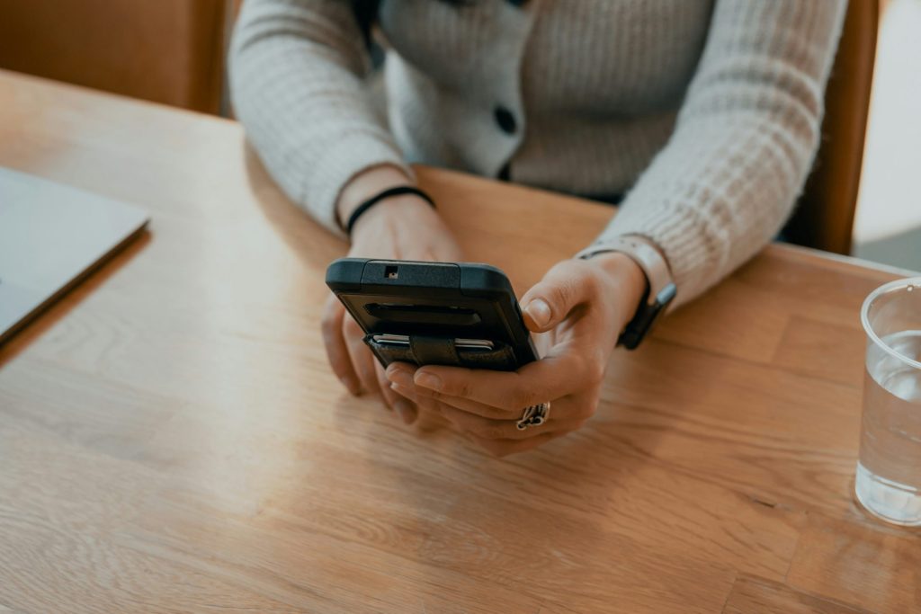 Frau im weißen Pullover hält schwarzes Smartphone