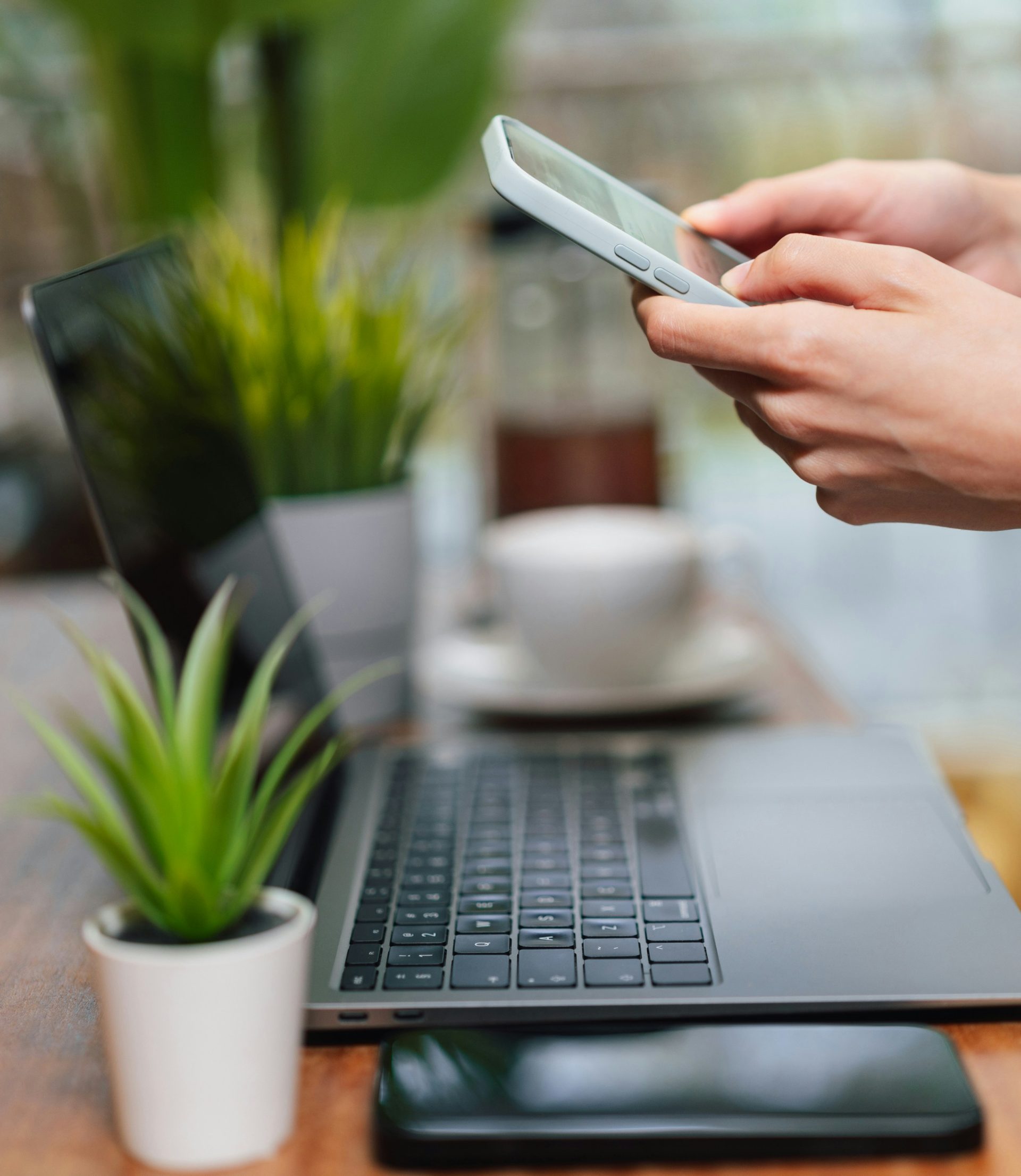 Person benutzt Telefon in der Nähe des Laptops auf dem Tisch.